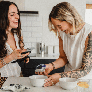 Two freelance social media managers creating content together in a bright kitchen, smiling while working on a food brand shoot