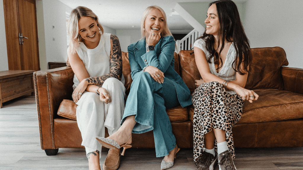 KW Marketing team members sitting on a leather sofa, smiling and chatting during a relaxed brand photoshoot in Exeter.